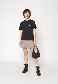 T-shirt en coton noir avec une poche poitrine ; jupe plissée beige ; bottes de combat noires ; petit sac à main noir avec une sangle.