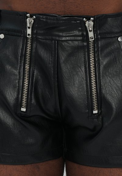 Schwarze Lederhosen mit auffälligen silbernen Reißverschlüssen auf der Vorderseite und einer glatten Textur. Das Design umfasst zwei mit Reißverschluss versehene Taschen.