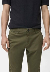 Khaki chinos featuring a slim fit, button closure, and front pockets. Fabric has a smooth texture with a subtle sheen.