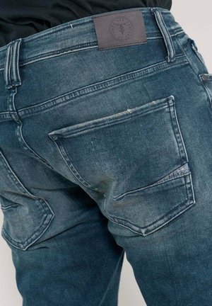 Jean en denim d'une couleur bleu délavé, coupe droite, deux poches arrière avec des surpiqûres contrastées, et une étiquette en cuir de marque à la taille.