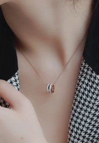 Sudraba kaklarota ar divām savienotām gredzeniem, viens ir pulēts zeltīts ar melniem akcentiem, bet otrs ir balts. Ķēde izskatās smalka un eleganta.