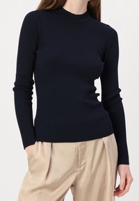 Ribbad långärmad topp i marinblått, med hög krage och slim fit. Materialet verkar mjukt med en strukturerad yta.