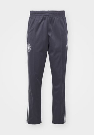 Navy athletic pants with an elastic waistband, white side stripes, and a circular logo on one leg. Made of lightweight, smooth fabric.
