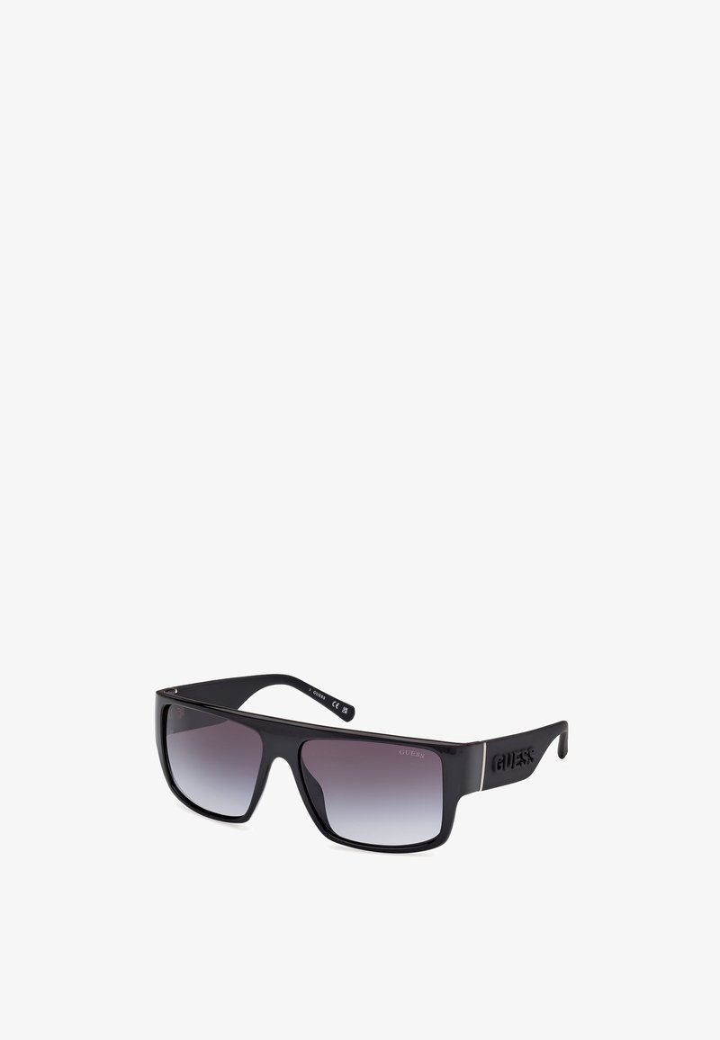 Lunettes de soleil noires surdimensionnées avec verres dégradés, finition lisse et logo bien en vue sur le côté de la branche. Conception de monture rectangulaire.