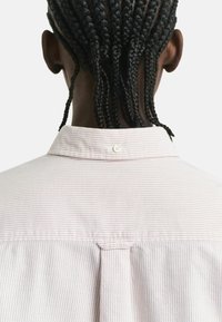Person with braided hair viewed from behind wearing a white and pink striped collared shirt with a back button detail.