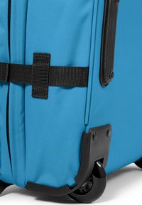 Valigia blu con ruote, caratterizzata da un tessuto testurizzato, accessori neri, una tracolla per un facile trasporto e robuste ruote in gomma per una maggiore mobilità.