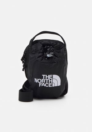 Kompaktowa czarna torba na ramię North Face z zapięciem na sznurek i białym logo na przodzie, na jednolitym białym tle.