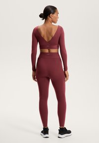 Bordeaux sportoutfit met een langarmige cropped top met een V-rug en hoge taille leggings, beide gemaakt van gladde, rekbare stof.