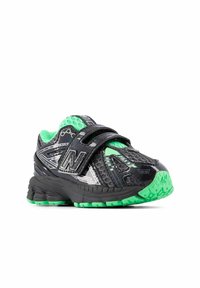 Zapato deportivo negro con acentos verdes, que presenta una parte superior sintética texturizada, un cierre de correa ajustable y una suela acolchada.