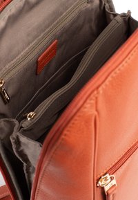 Binnenkant van een tan leren tas met meerdere ritszakken. Kenmerkt een gladde textuur, gouden hardware en een logo label op de stofvoering.