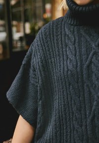 Kuscheliger Strickpullover aus dunkelblauer Wolle mit hohem Kragen und kurzen Ärmeln, ausgestattet mit einem Zopfmuster und strukturierten Details.