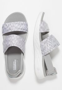 Sandali Skechers grigi e bianchi con due cinturini in tessuto fantasia, soletta imbottita e cinturino per il tallone regolabile, mostrati in vista dall'alto e di lato.