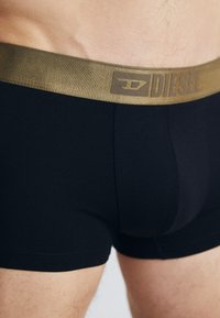 Black cotton boxer briefs with a textured gold waistband featuring the "DIESEL" logo. Close-up view highlights fit and material.