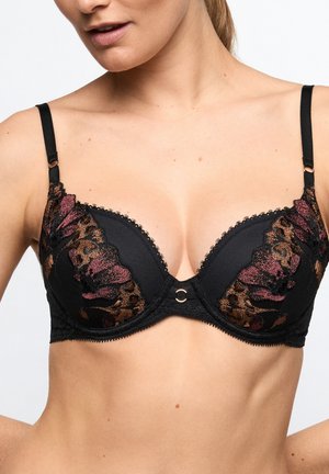 Frau trägt schwarzen BH mit floraler und Leoparden-Spitzenstickerei, verstellbaren Trägern und kleinem zentralem Ringdetail.