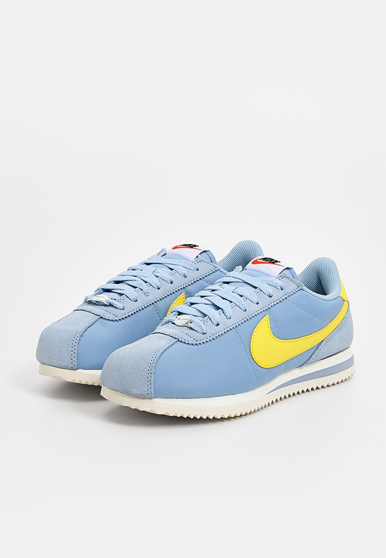 Baskets bleu clair avec un embout en suède et un swoosh jaune, dotées d'accents gris, d'une semelle intermédiaire blanche et d'une semelle extérieure en caoutchouc texturé.
