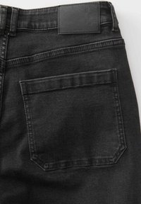 Vista posteriore di jeans in denim nero che mostrano una tasca posteriore e una vita cucita con una etichetta in pelle nera.