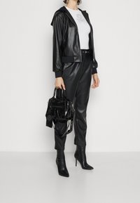 Felpa con zip in ecopelle nera, t-shirt bianca con grafiche, pantaloni in ecopelle nera coordinati, décolleté e borsa testurizzata.