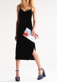 Musta samettimekko, jossa on spagettihihnat ja sivuletku; malli pitää hopeista käsilaukkua, jossa on punaisia ja sinisiä tähtikuvioita; siniset korot.