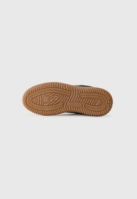 Sole di sneaker nera con un design in gomma naturale testurizzata, caratterizzata da scanalature e dal logo "PUMA". Forma pulita e funzionale.