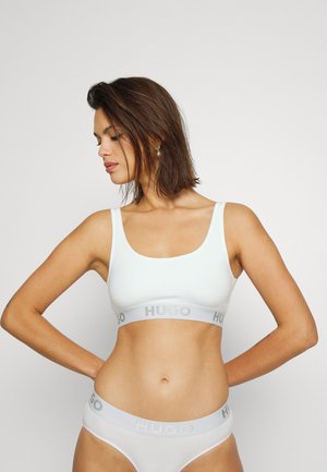 Bralette bianco con una texture liscia, dotata di un elastico grigio con logo. Abbinato a slip hipster bianchi coordinati.