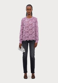 Suéter lavanda con un diseño floral texturizado, combinado con jeans oscuros y un bolso de mano plateado. Las capas transparentes crean un efecto suave y dimensional.