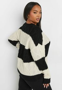 Svart och krämrandig tröja med en chunky stickad mönster, ribbade ärmslut och rund halsringning, med en avslappnad passform och texturerad design.