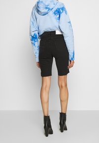 Mustat farkkushortsit rosoisella helmalla, yhdistettynä vaaleansinsiseen siteeraus-huppariin ja mustiin nilkkurit, joissa on paksu korko.