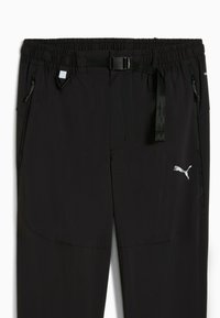 Zwarte sportbroek met elastische tailleband, verstelbare riem en zakken met rits. Heeft een wit Puma-logo aan de linkerkant.