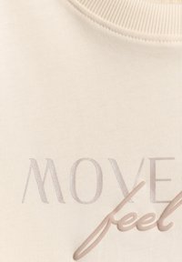 Tissu beige avec col côtelé et texte « MOVE feel » imprimé en tons marron doux et violet clair.