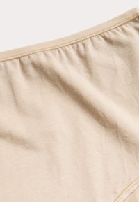 Beige stof met een gladde textuur en een lichte stretch; beschikt over een gathered elastiek aan de bovenkant voor een veilige pasvorm.