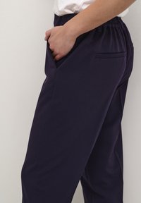 Pantalons bleu marine extensibles avec une taille élastique, dotés de poches latérales et d'une texture lisse. Design minimaliste avec des lignes épurées.