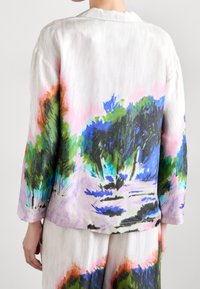 Lätt, flerfärgad linjacka med en naturinspirerad design med gröna och blå bladverk på en ljus bakgrund. Långa ärmar, avslappnad passform.