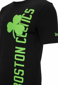 Camiseta de algodón negra con un gran trébol verde y el texto vertical "BOSTON CELTICS". Acentos en neón verde notables. Cuello redondo.