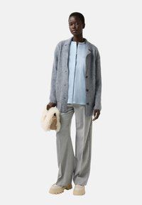 Cardigan gris duveteux sur une chemise bleu clair, associé à un pantalon large gris clair et des chaussures à plateforme crème. Tenant un petit sac en fourrure.