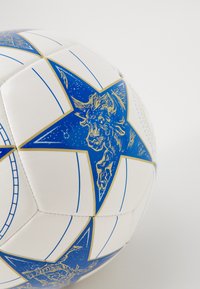 Biely futbalový lopt s modrými hviezdami a zlatými akcentmi, ilustrovanou hlavou býka, textúrovaným povrchom a šitými panelmi.