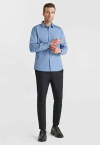 Lichtblauwe gebloemde button-up shirt, slanke zwarte broek en zwarte schoenen. Het shirt heeft een kraag en manchetdetails.