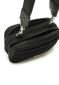 Schwarze Umhängetasche mit zwei Reißverschlussfächern, strukturiertem Stoff und einem verstellbaren Riemen mit einem gesteppte Lederakzent.