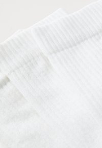Chaussettes blanches côtelées en tissu doux, présentant une texture lisse avec un revers replié en haut et des bords nets.
