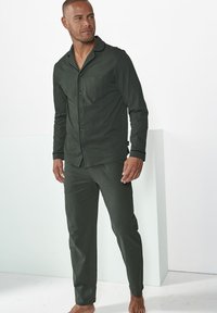 Men's dark green pajama set made of soft fabric, featuring a button-up shirt with a pocket and long pants, accented with black trim.