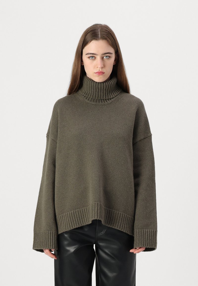 Overdimensjonert olivenfarget genser med høy hals, strikket tekstur, stripete mansjetter og nederkant, brukt sammen med høyt liv svart skinnbukser.