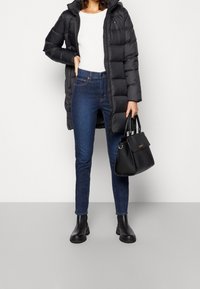 Svart puffjacka med huva, vit ribbad tröja, mörkblå slim jeans, svarta ankelstövlar och en strukturerad svart handväska.