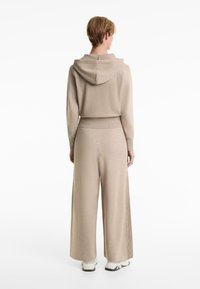 Beige knit hoodie with a wide collar, ribbed cuffs and waistband, paired with matching wide-leg pants. Smooth texture with subtle sheen.