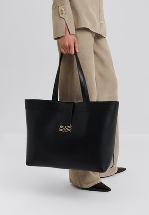 Sac cabas en cuir noir au design structuré, doté d'une sangle avant et de détails en métal doré. Texture lisse et longues anses en cuir.