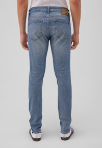 Light blue denim jeans with a straight leg design, featuring back pockets and a tan brand patch at the waistband.