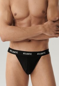 Czarne stringi z szerokim elastycznym paskiem w białym kolorze z logo "ATLANTIC". Gładki materiał, dopasowany krój, minimalistyczny styl.