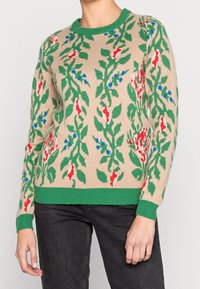 Pull en tricot beige avec des motifs floraux vibrants en vert, rouge et bleu. Il possède un col rond et des poignets et un ourlet côtelés en vert.