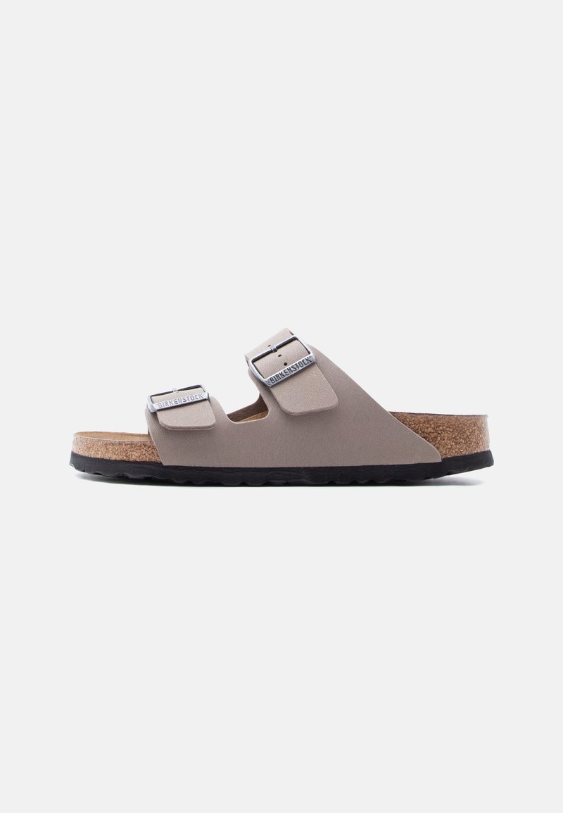 Μπεζ σανδάλι Birkenstock με δύο λουριά και ασημένια αγκράφες, πάτο από φελλό και μαύρη υφή στην σόλα, εμφανίζεται σε πλευρική όψη σε λευκό φόντο.