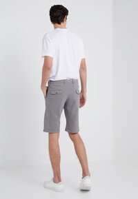 Pantaloni corti grigi con una vestibilità comoda, due tasche posteriori e orlo piegato, abbinati a una maglietta bianca semplice e sneakers bianche.