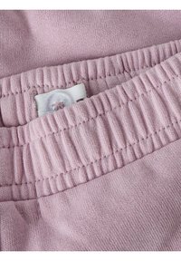 Jasnoróżowa tkanina o miękkiej fakturze, z marszczonym paskiem w talii i detalem zapinanym na guzik. Zbliżenie na przeszycia w materiale.