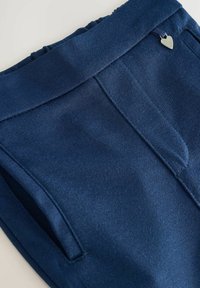 Donkerblauwe broek met een gladde textuur, voorzien van een brede tailleband, zijkleine zakken en een kleine hartvormige metalen accent.